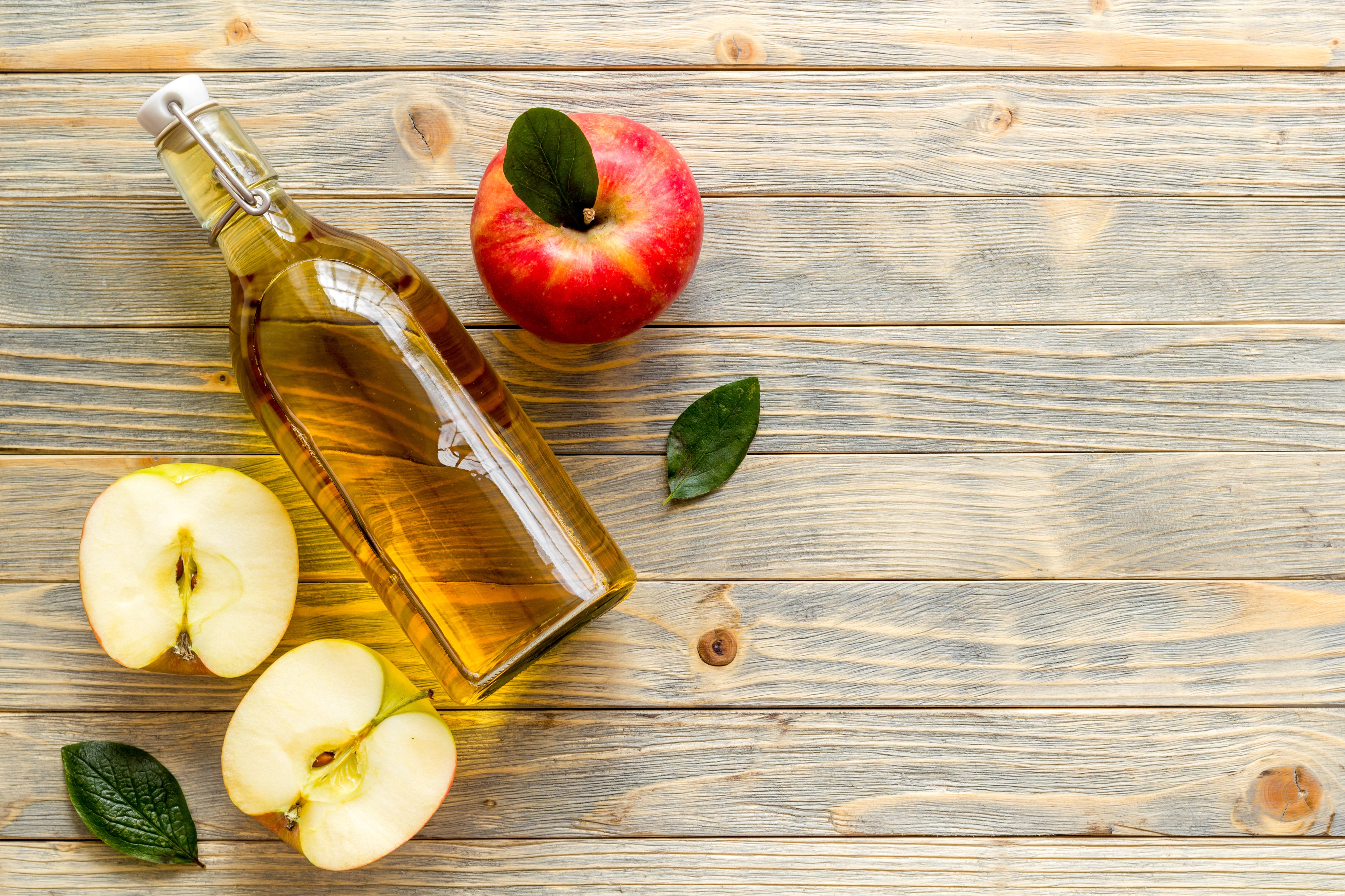 Top-down view of a bottle of apple cider vinegar with apples and slices on a rustic wooden surface