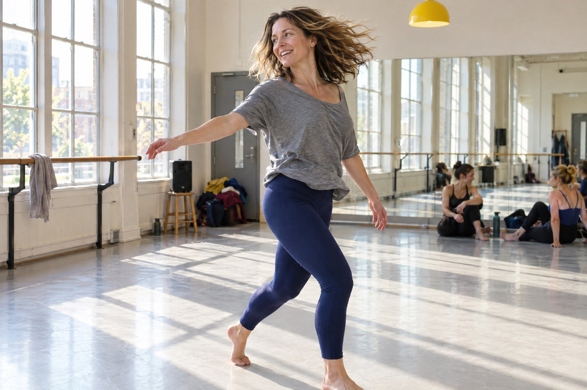 A woman turns mid-dance in a bright studio under a yellow pendant lamp.