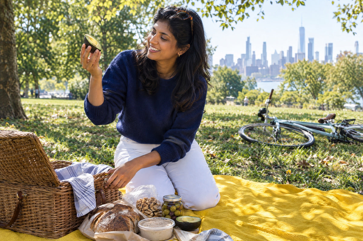 A woman unpacks a picnic on a yellow blanket in a sunny park.