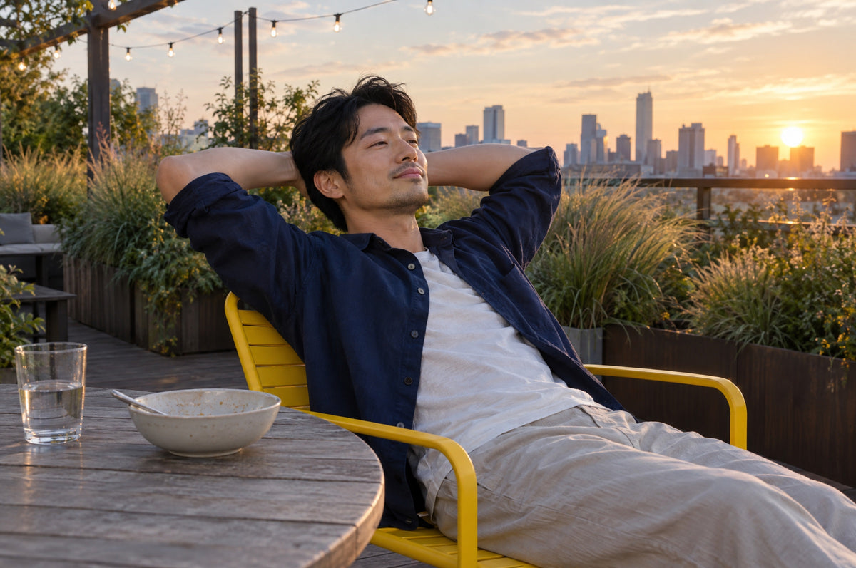 A man relaxes in a yellow chair on a rooftop terrace at golden hour after dinner.